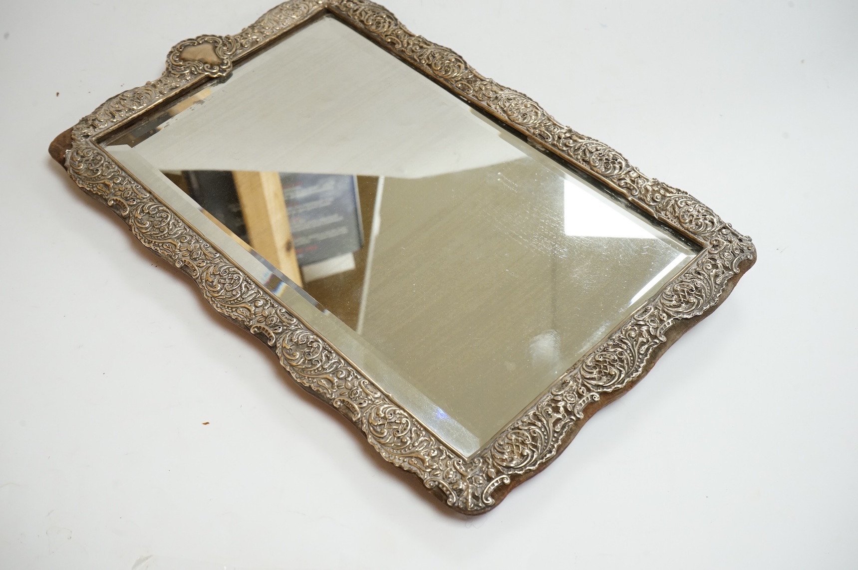 A late Victorian repousse silver mounted rectangular easel mirror, Birmingham, 1896, 35.7cm(a.f.), together with a modern silver mounted photograph frame, a silver handbag mirror/compact, three mounted glass toilet jars,